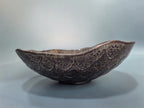 A dark brown ceramic bowl with a textured, scalloped exterior and a glossy finish, set against a soft gray background.