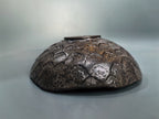 A dark brown ceramic bowl with a textured, embossed floral pattern and a small top handle, photographed against a neutral gray background.