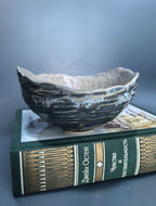 A handmade ceramic bowl with a rustic, organic rim sits on top of a green book against a dark gray background.