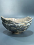 A handmade ceramic bowl with a textured, ribbed exterior and a cracked, glossy interior, shown on a neutral gray background.