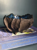 A dark brown, textured ceramic bowl with a blue glazed interior, displayed on top of a blue book.