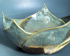 A close-up of a ceramic bowl with a lotus-petal-inspired design, featuring a glossy glaze in shades of teal, olive green, and gold, with a dark brown base.
