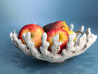 A white coral-shaped ceramic bowl filled with red and yellow apples, set against a smooth blue background.